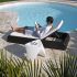 Propriétaire détendu sur une chaise longue au bord de sa piscine, illustrant la sérénité offerte par un logement bien sécurisé pendant les vacances d’été.